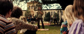 Movie still from “Jesus Revolution” (2023), directed by Brent McCorkle – A man standing in the middle of a park with a microphone; Wide shot, Over the shoulder angle