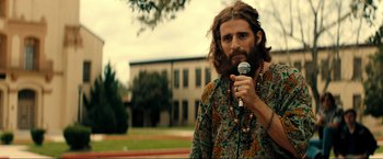 Movie still from “Jesus Revolution” (2023), directed by Brent McCorkle – A man with long hair holding a microphone in his hand; Medium shot, Over the shoulder angle
