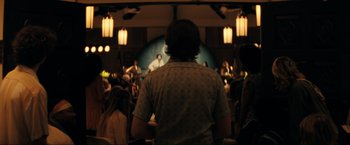 Movie still from “Jesus Revolution” (2023), directed by Brent McCorkle – A man standing in front of an audience in front of a microphone; Medium shot, Over the shoulder angle