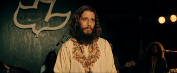 Movie still from “Jesus Revolution” (2023), directed by Brent McCorkle – A man with long hair and a beard wearing a white robe; Medium shot, Over the shoulder angle