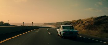 Movie still from “Jesus Revolution” (2023), directed by Brent McCorkle – A car driving down a road next to the ocean; Wide shot, High angle