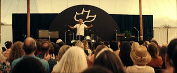 Movie still from “Jesus Revolution” (2023), directed by Brent McCorkle – A man standing in front of a crowd of people; Wide shot, Over the shoulder angle