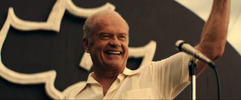 Movie still from “Jesus Revolution” (2023), directed by Brent McCorkle – An older man with a goatee smiling for the camera; Medium shot, Low angle