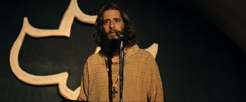 Movie still from “Jesus Revolution” (2023), directed by Brent McCorkle – A man with long hair and a beard is holding a microphone; Medium shot, Low angle
