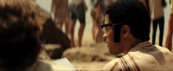 Movie still from “Jesus Revolution” (2023), directed by Brent McCorkle – A man sitting on the beach reading a book; Close Up shot, Over the shoulder angle