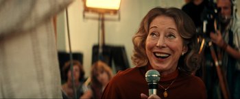 Movie still from “Jesus Revolution” (2023), directed by Brent McCorkle – An older woman is holding a microphone in her hand; Close Up shot, Over the shoulder angle