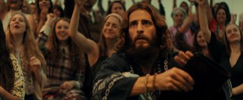 Movie still from “Jesus Revolution” (2023), directed by Brent McCorkle – A man with long hair and a beard in a crowd of onlookers; Medium shot, Low angle