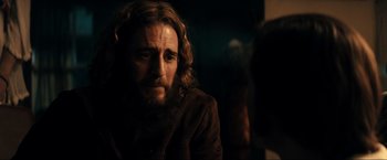 Movie still from “Jesus Revolution” (2023), directed by Brent McCorkle – A man with long hair and a beard is sitting in a dark room; Close Up shot, Over the shoulder angle