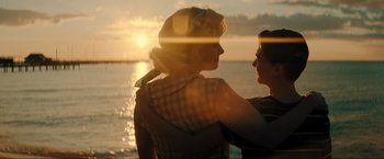 Movie still from “Jesus Revolution” (2023), directed by Brent McCorkle – Two women standing next to a body of water at sunset; Medium shot, Over the shoulder angle
