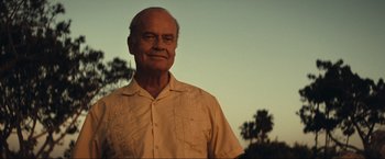 Movie still from “Jesus Revolution” (2023), directed by Brent McCorkle – An older man wearing a tan shirt and palm trees in the background; Close Up shot, Low angle