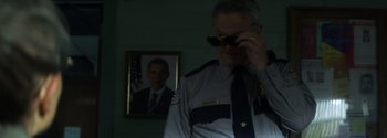 Movie still from “Joe Bell” (2020), directed by Reinaldo Marcus Green – A man in a police uniform standing in front of a picture of president obama; Close Up shot, Over the shoulder angle