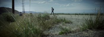 Movie still from “Joe Bell” (2020), directed by Reinaldo Marcus Green – A man walking across a dirt road near a field; Wide shot, Low angle