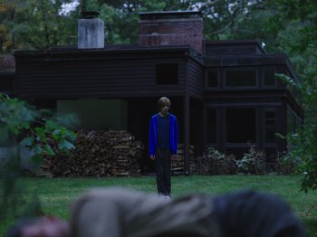 Movie still from “John and the Hole” (2021), directed by Pascual Sisto – A man standing in a yard near a house; Wide shot, Over the shoulder angle