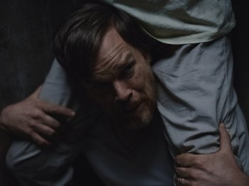Movie still from “John and the Hole” (2021), directed by Pascual Sisto – A bearded man with a beard is holding on to another man's shirt; Medium shot, Overhead angle