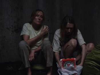 Movie still from “John and the Hole” (2021), directed by Pascual Sisto – Two women sitting on the ground looking at a bag of food; Medium shot, High angle