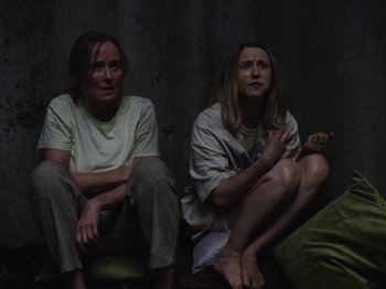 Movie still from “John and the Hole” (2021), directed by Pascual Sisto – Two women sitting on the ground in front of a wall; Medium shot, Overhead angle