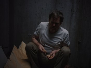 Movie still from “John and the Hole” (2021), directed by Pascual Sisto – A man sitting on the ground eating something; Medium shot, High angle