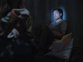 Movie still from “John and the Hole” (2021), directed by Pascual Sisto – A man sitting on the ground in a dark room; Medium shot, High angle