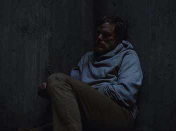 Movie still from “John and the Hole” (2021), directed by Pascual Sisto – A man sitting on the ground holding a cell phone; Medium shot, High angle