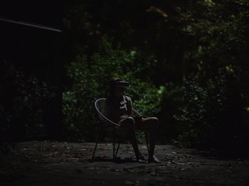 Movie still from “John and the Hole” (2021), directed by Pascual Sisto – A person sitting on a chair in the dark; Extreme Wide shot, Low angle