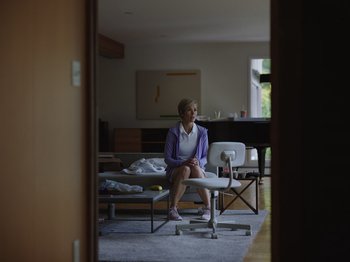 Movie still from “John and the Hole” (2021), directed by Pascual Sisto – An older woman sitting on a chair in a living room; Wide shot, Low angle