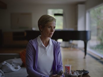 Movie still from “John and the Hole” (2021), directed by Pascual Sisto – A woman sitting at a table with a drink; Medium shot, Low angle