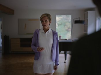 Movie still from “John and the Hole” (2021), directed by Pascual Sisto – A woman standing in a living room holding a cell phone; Medium shot, Over the shoulder angle