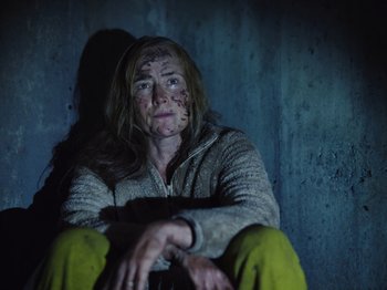 Movie still from “John and the Hole” (2021), directed by Pascual Sisto – A woman sitting on the ground in the dark; Medium shot, High angle