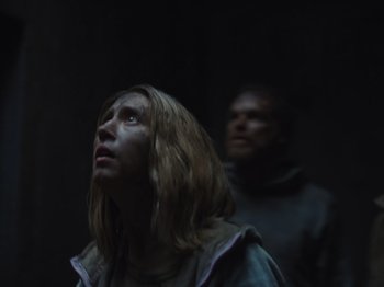 Movie still from “John and the Hole” (2021), directed by Pascual Sisto – A woman and a man are standing in a dark room looking up; Medium shot, Low angle