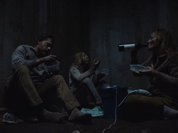 Movie still from “John and the Hole” (2021), directed by Pascual Sisto – A group of people sitting on the ground in a dark room; Wide shot, Low angle