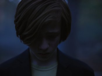 Movie still from “John and the Hole” (2021), directed by Pascual Sisto – A person with a black jacket is looking at the camera; Close Up shot, High angle