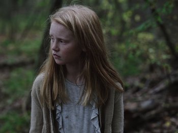 Movie still from “John and the Hole” (2021), directed by Pascual Sisto – A young girl is standing in the woods; Close Up shot, Over the shoulder angle