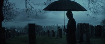 Movie still from “John Wick” (2014), directed by Chad Stahelski – A person holding an umbrella in a cemetery; Wide shot, Low angle
