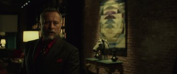 Movie still from “John Wick” (2014), directed by Chad Stahelski – A man in a suit sitting in front of a painting; Medium shot, Over the shoulder angle