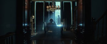 Movie still from “John Wick” (2014), directed by Chad Stahelski – A person sitting at a table in a room with chandeliers; Extreme Wide shot, Low angle