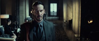 Movie still from “John Wick” (2014), directed by Chad Stahelski – A man in a suit and tie standing in a room; Medium shot, Low angle