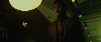 Movie still from “John Wick” (2014), directed by Chad Stahelski – A man in a suit and tie standing in front of a light; Medium shot, Low angle