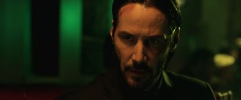 Movie still from “John Wick” (2014), directed by Chad Stahelski – A man in a suit and a green light in the background; Close Up shot, Low angle