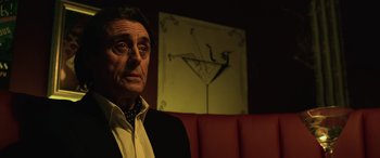 Movie still from “John Wick” (2014), directed by Chad Stahelski – A man sitting in front of a picture of a martini glass; Close Up shot, Low angle