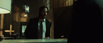 Movie still from “John Wick” (2014), directed by Chad Stahelski – A man wearing a suit and tie standing in front of a table; Medium shot, Over the shoulder angle