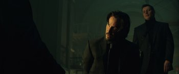 Movie still from “John Wick” (2014), directed by Chad Stahelski – A man wearing a suit and tie in a dark room; Medium shot, Over the shoulder angle