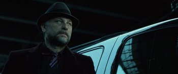 Movie still from “John Wick” (2014), directed by Chad Stahelski – A man wearing a hat and a suit and tie next to a car; Close Up shot, Low angle