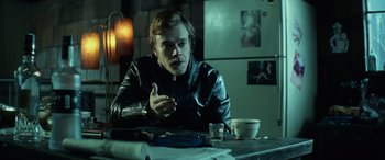 Movie still from “John Wick” (2014), directed by Chad Stahelski – A man sitting at a table in a dark room; Medium shot, Over the shoulder angle