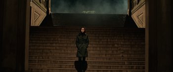 Movie still from “John Wick” (2014), directed by Chad Stahelski – A woman standing on some steps wearing a green coat; Wide shot, Low angle