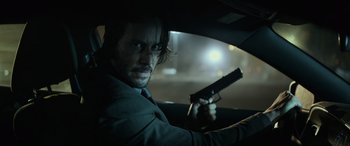 Movie still from “John Wick” (2014), directed by Chad Stahelski – A man holding a gun while sitting in a car; Close Up shot, Low angle