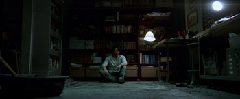 Movie still from “John Wick: Chapter 2” (2017), directed by Chad Stahelski – A man sitting on the floor in a room with books; Wide shot, Overhead angle
