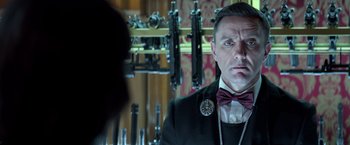 Movie still from “John Wick: Chapter 2” (2017), directed by Chad Stahelski – A man wearing a suit and tie in a room with guns; Close Up shot, Over the shoulder angle