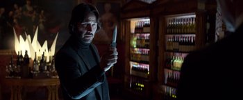 Movie still from “John Wick: Chapter 2” (2017), directed by Chad Stahelski – A man holding a knife in a room full of bottles; Medium shot, Low angle