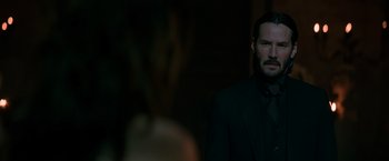Movie still from “John Wick: Chapter 2” (2017), directed by Chad Stahelski – A man wearing a suit and tie standing in front of a wall; Close Up shot, Over the shoulder angle