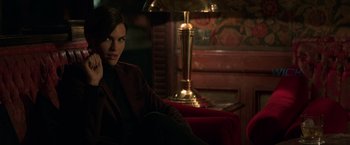 Movie still from “John Wick: Chapter 2” (2017), directed by Chad Stahelski – A woman sitting on a red chair next to a lamp; Medium shot, Over the shoulder angle